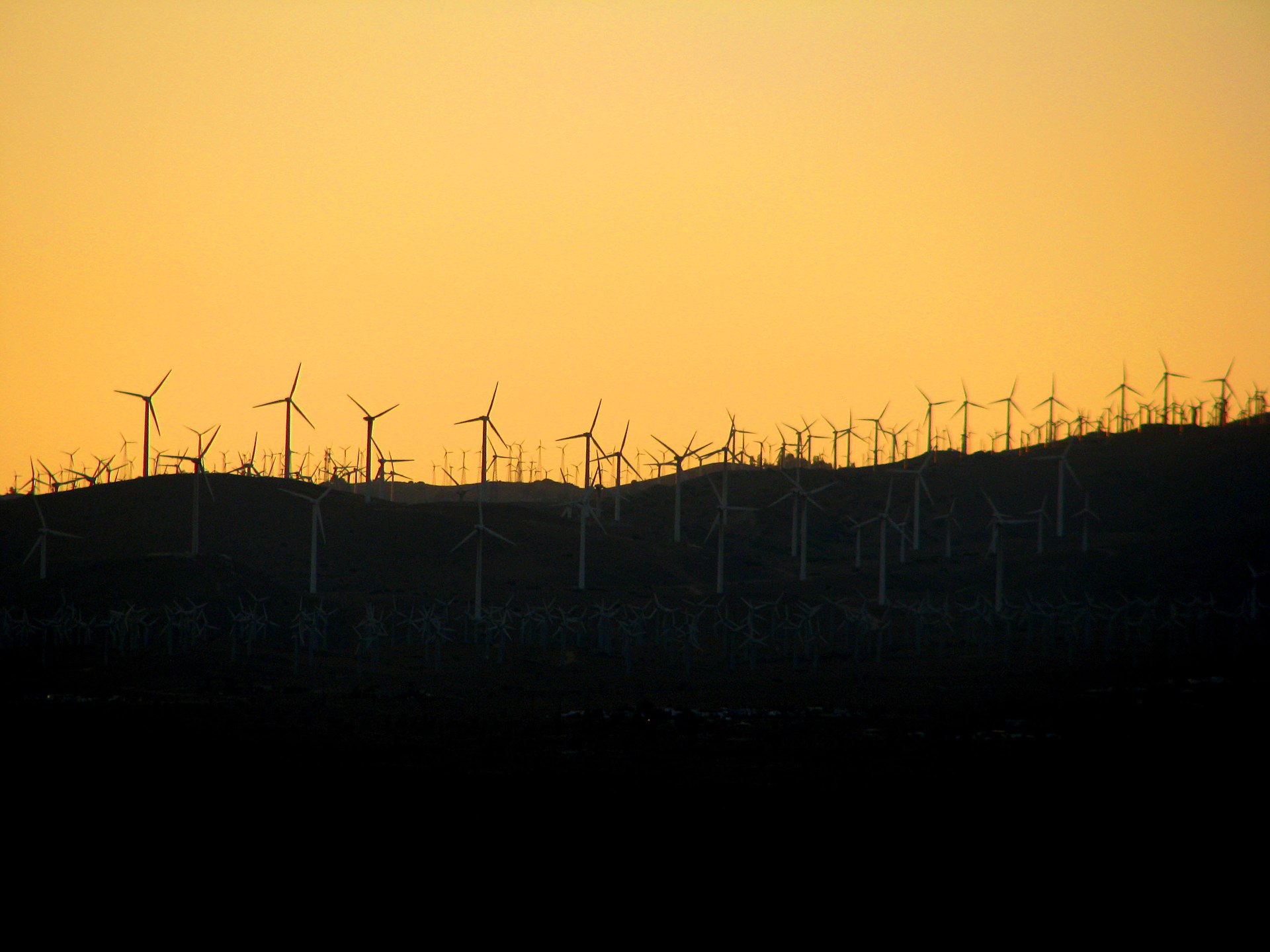 Wind turbines silhouetted against a golden sunset sky in the Tehachapi hills
